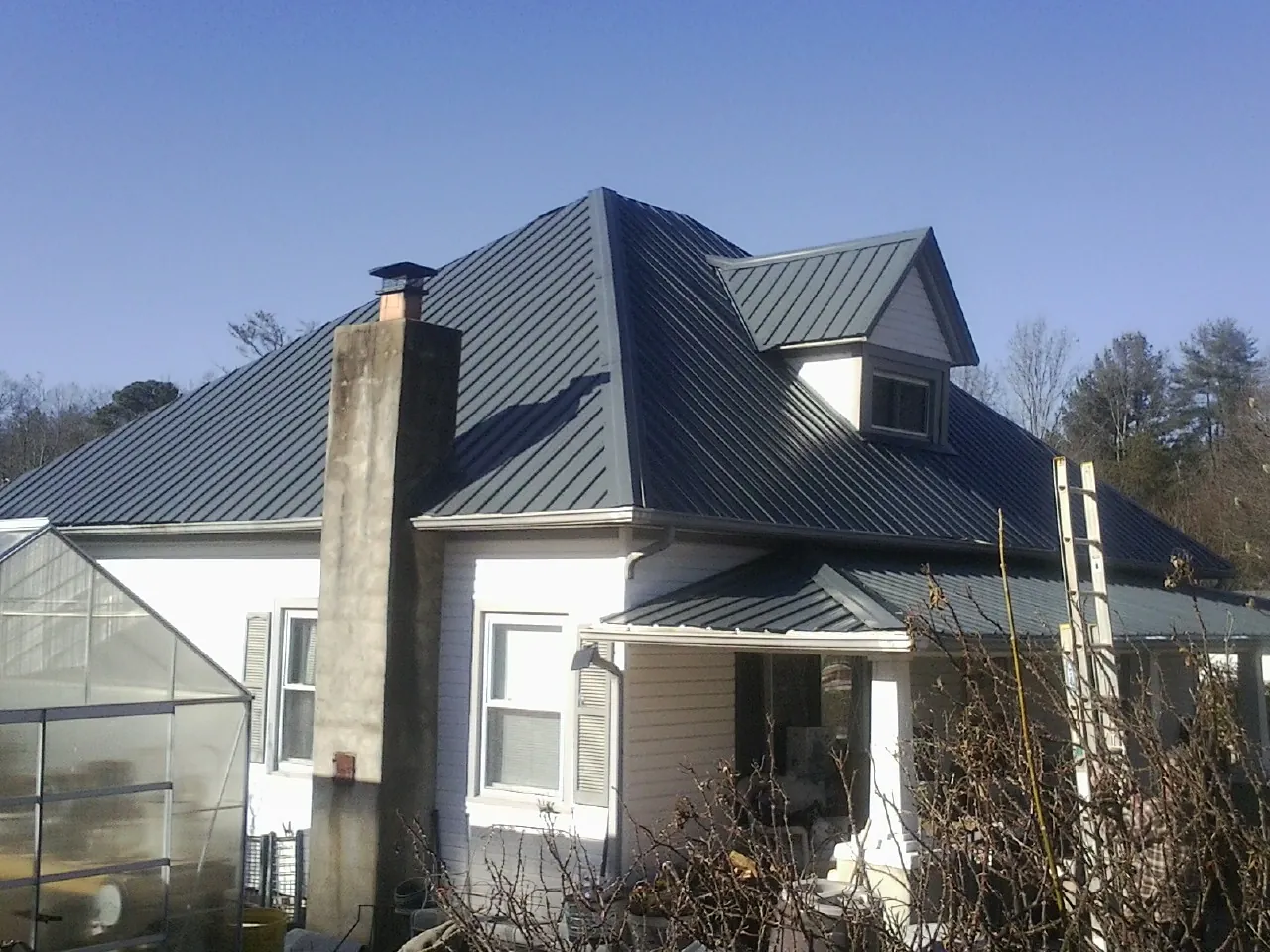 Dark blue standing seam metal roof on a white farmhouse with dormer — Slate & Tile Roof Repair by Roofing Brothers in Eidson