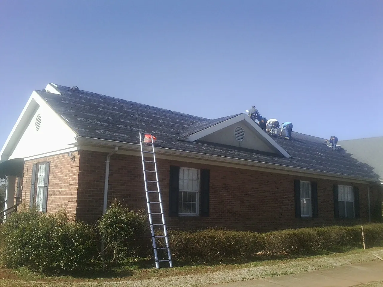 Crew tearing shingles off a brick ranch roof with a ladder set — Emergency Roof Repair work by our crew in Eidson