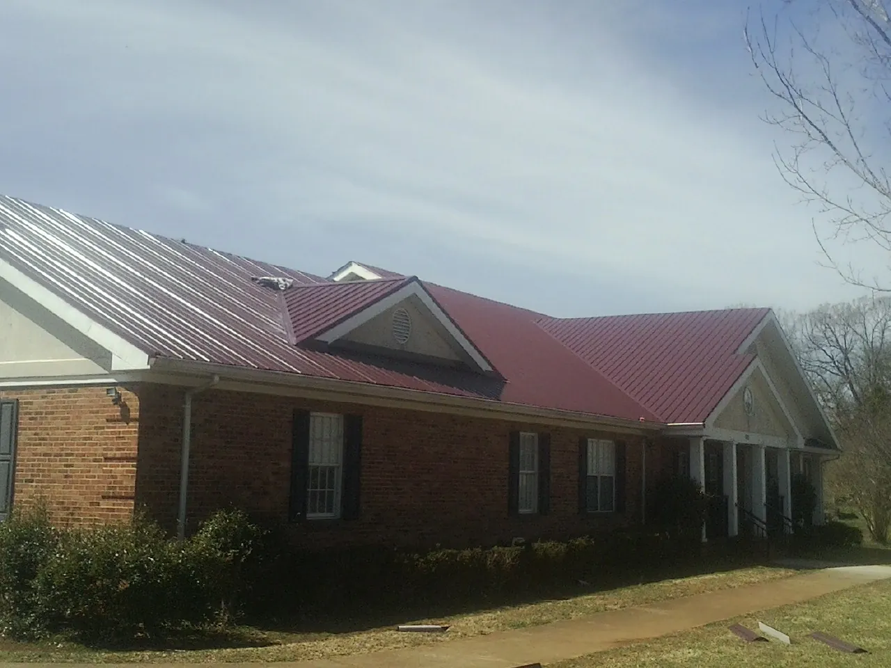 Red metal roof with gabled entries on a long brick building, from a Hail Damage Roof Repair job in Eidson