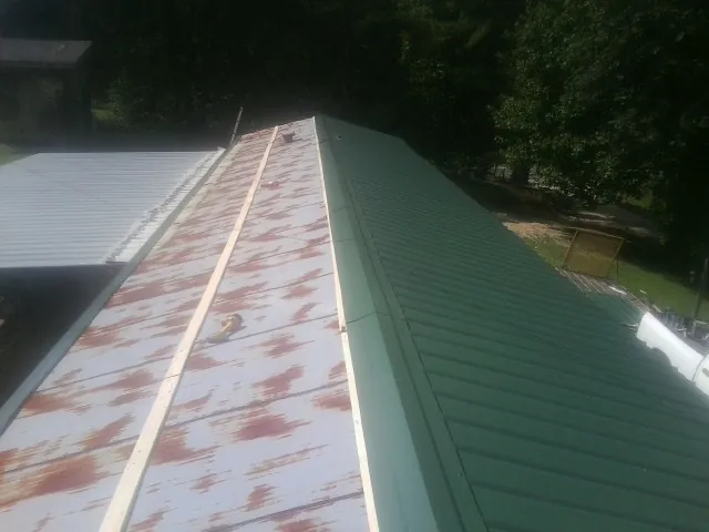 Old rusted panels beside newly installed green metal roofing — Wind Damage Roof Repair by Roofing Brothers in Eidson