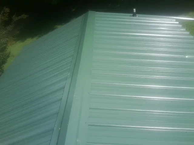 New green metal panels meeting at the ridge of a roof — Flat Roof Repair work by our crew in Eidson