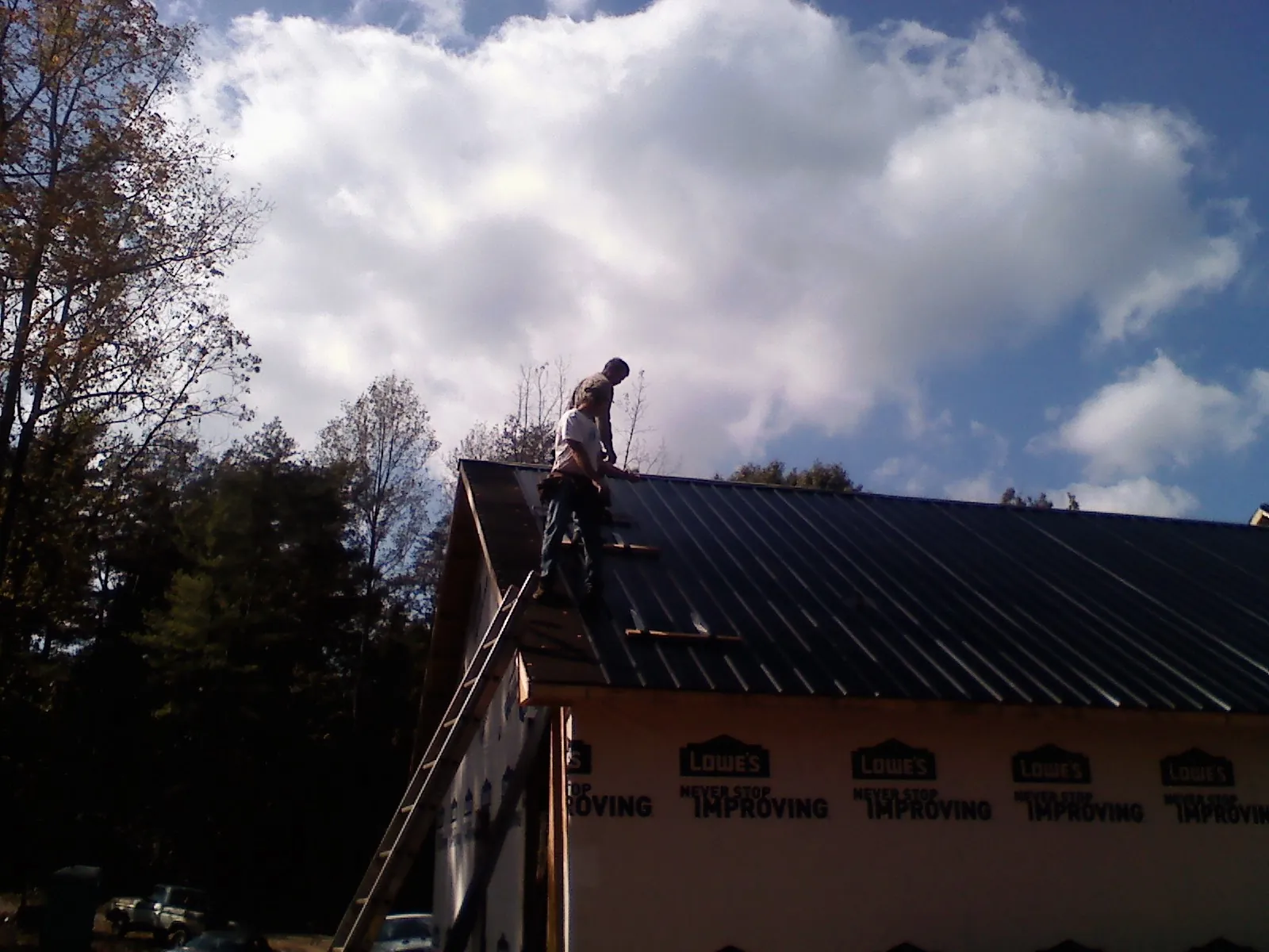 Roofer fastening dark metal panels high against a cloudy sky, from a Roof Inspection job in Eidson