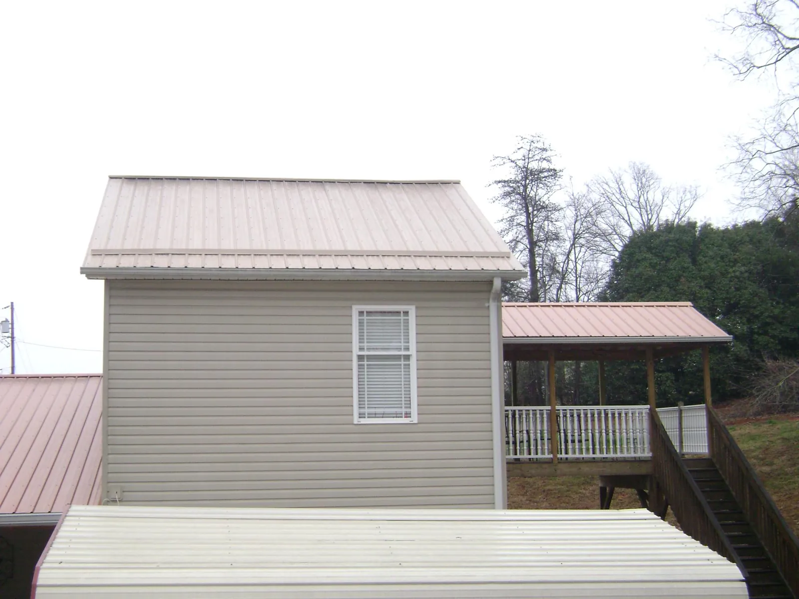 Tan metal roofs on a two story addition and attached porch, from a Roof Replacement job in Eidson